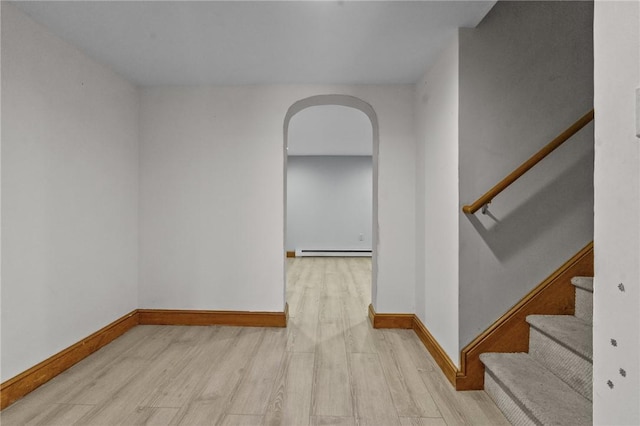 spare room featuring light wood finished floors, baseboards, arched walkways, stairs, and a baseboard heating unit