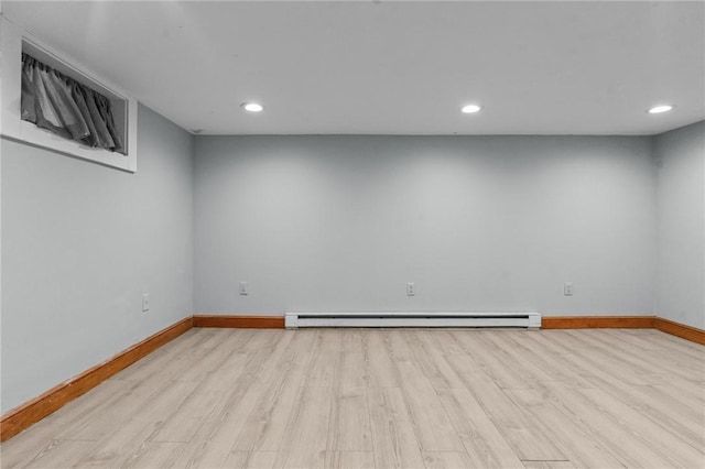 below grade area with baseboard heating, light wood-type flooring, and baseboards