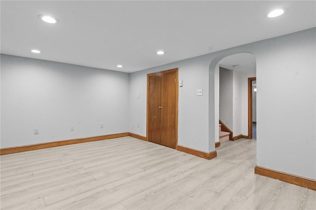 unfurnished room with arched walkways, baseboards, light wood finished floors, and recessed lighting