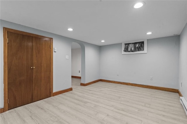 finished basement featuring arched walkways, recessed lighting, light wood-style floors, a baseboard heating unit, and baseboards