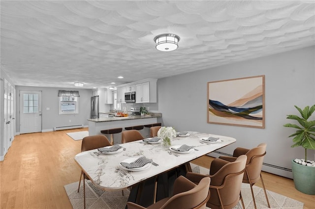 dining space featuring light wood-type flooring, a baseboard radiator, a textured ceiling, and baseboard heating