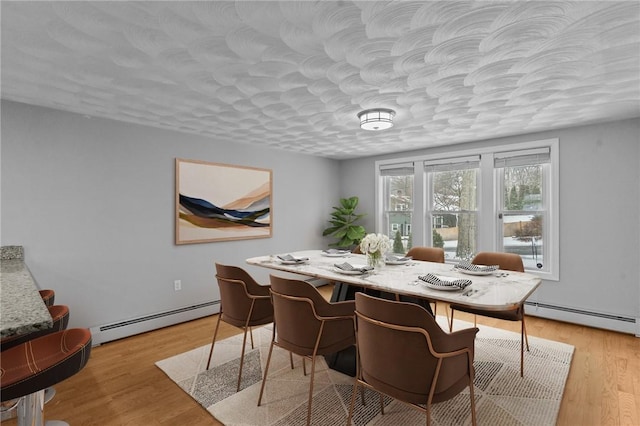 dining space featuring light wood-style flooring, baseboard heating, and a textured ceiling