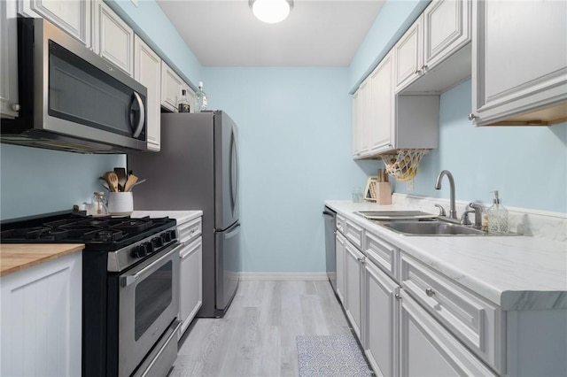 kitchen with light wood-style flooring, stainless steel appliances, wood counters, a sink, and baseboards