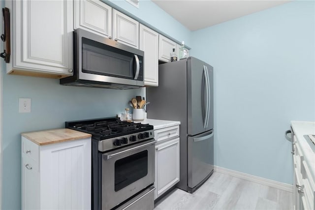 kitchen featuring light wood-style floors, baseboards, appliances with stainless steel finishes, and white cabinets