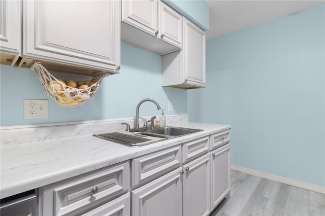 kitchen with light wood finished floors, baseboards, white cabinetry, and a sink