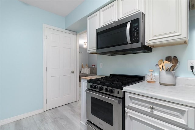 kitchen with baseboards, white cabinets, light stone countertops, stainless steel appliances, and light wood-type flooring