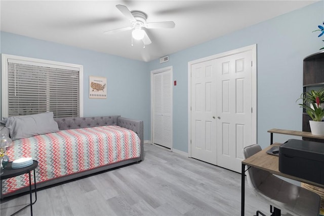 bedroom with ceiling fan, light wood-style flooring, visible vents, multiple closets, and baseboards