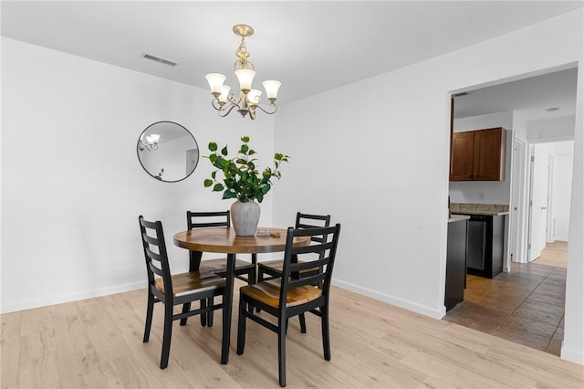 dining space with baseboards, light wood finished floors, visible vents, and an inviting chandelier