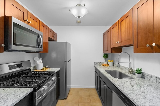 kitchen featuring stainless steel appliances, a sink, light stone countertops, and brown cabinets