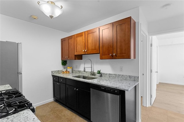 kitchen with appliances with stainless steel finishes, brown cabinetry, a sink, and light stone counters