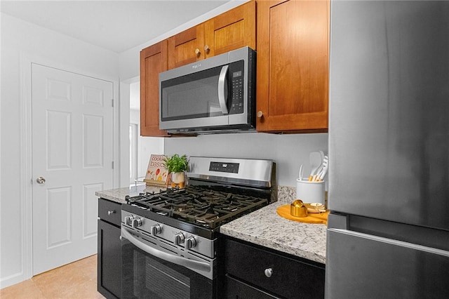 kitchen featuring brown cabinets, light tile patterned floors, light stone counters, and stainless steel appliances