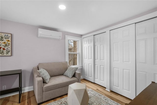 sitting room with light wood-type flooring, baseboards, an AC wall unit, and recessed lighting