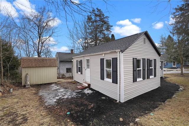 view of side of home featuring an outbuilding, a storage unit, a shingled roof, and entry steps