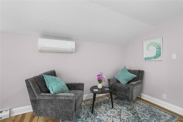 sitting room featuring a baseboard heating unit, an AC wall unit, vaulted ceiling, wood finished floors, and baseboards