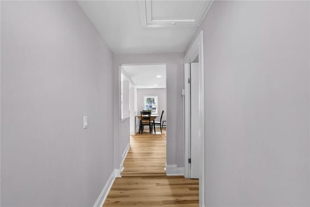 corridor with light wood finished floors, attic access, and baseboards