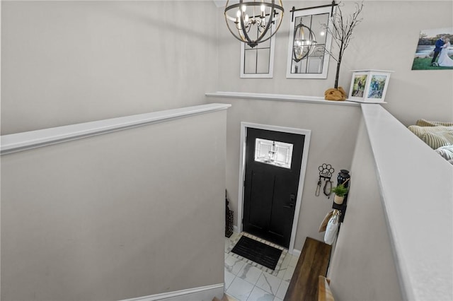 foyer entrance featuring a chandelier, marble finish floor, and baseboards