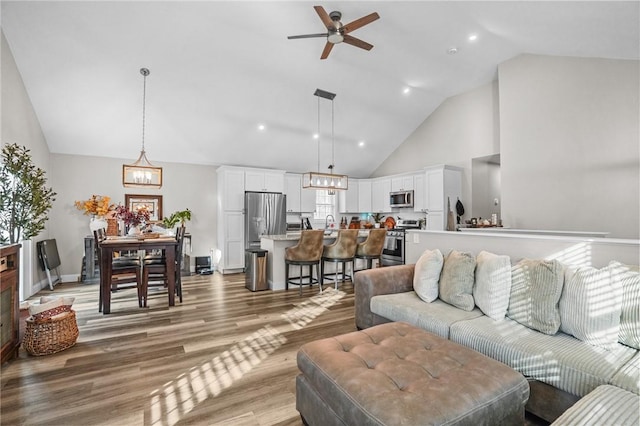 living room featuring baseboards, wood finished floors, ceiling fan with notable chandelier, high vaulted ceiling, and recessed lighting