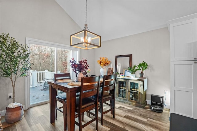 dining space with light wood-style floors, a chandelier, high vaulted ceiling, and baseboards