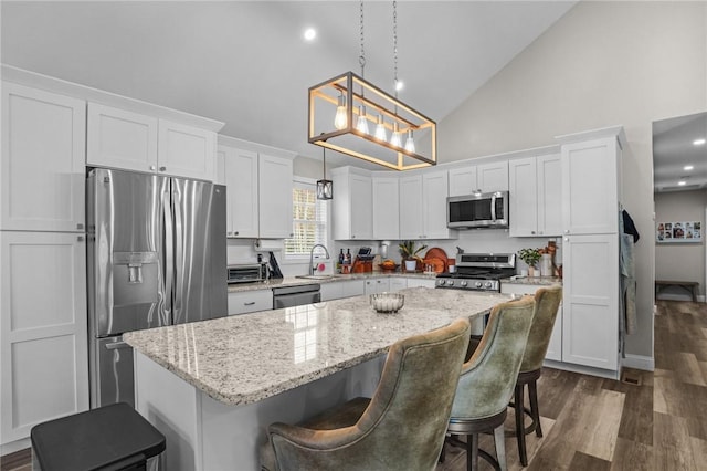 kitchen featuring a kitchen island, appliances with stainless steel finishes, white cabinets, and decorative light fixtures