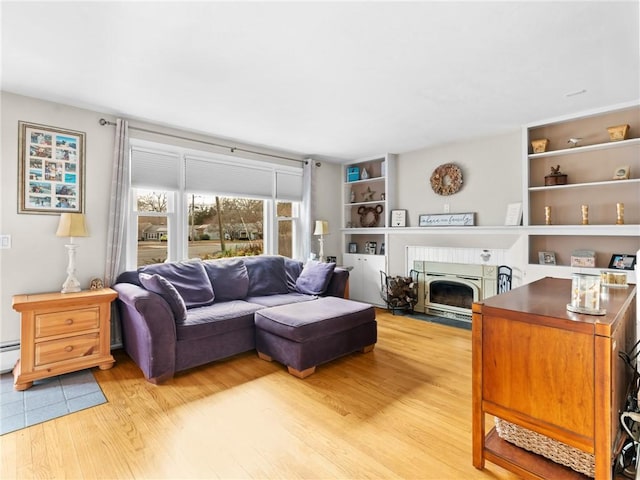 living room with built in shelves, baseboard heating, light wood-type flooring, and a fireplace with flush hearth