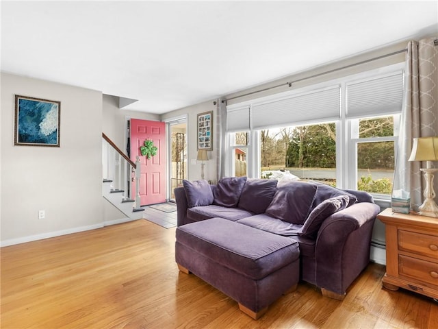 living room with a baseboard heating unit, light wood-type flooring, baseboards, and stairs