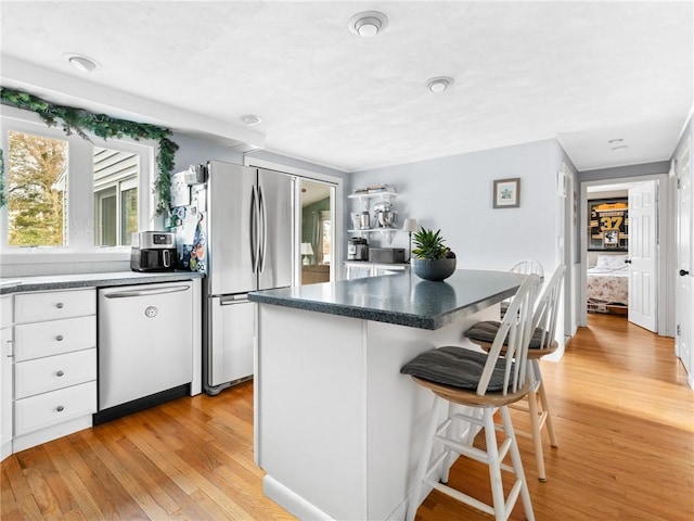 kitchen featuring a center island, a breakfast bar area, appliances with stainless steel finishes, light wood-style floors, and white cabinets