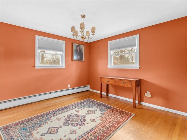 spare room featuring a chandelier, a baseboard radiator, baseboards, and wood finished floors