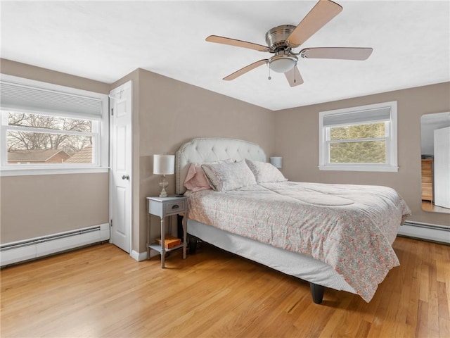 bedroom with light wood-style flooring, multiple windows, and a baseboard heating unit