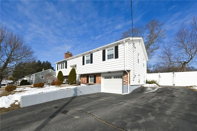 raised ranch with aphalt driveway, brick siding, a chimney, an attached garage, and fence