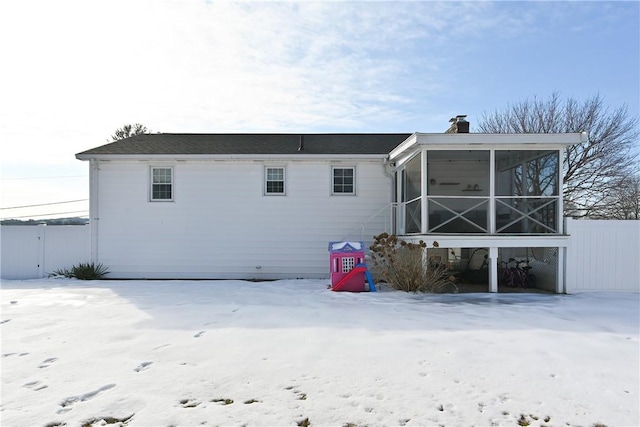 snow covered house with a chimney, fence, and a sunroom