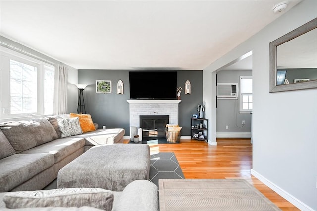 living room featuring a brick fireplace, baseboards, baseboard heating, and wood finished floors