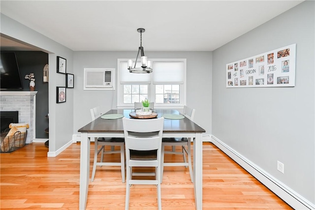 dining area with a chandelier, a wall unit AC, wood finished floors, a fireplace, and a baseboard heating unit