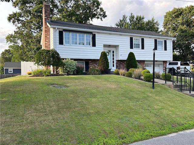 split foyer home with entry steps, an attached garage, brick siding, a chimney, and a front yard