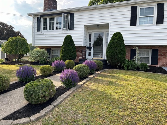 split foyer home featuring a chimney, a front lawn, and brick siding