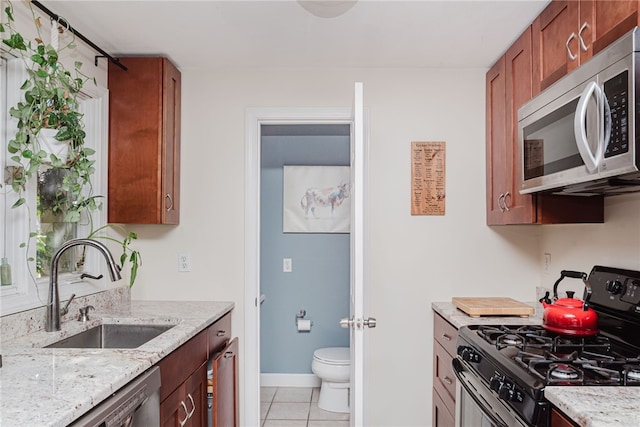 kitchen with light tile patterned floors, light stone counters, a sink, baseboards, and appliances with stainless steel finishes