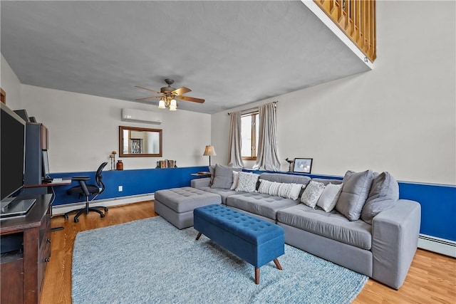 living area with a ceiling fan, a baseboard heating unit, wood finished floors, and a wall mounted air conditioner