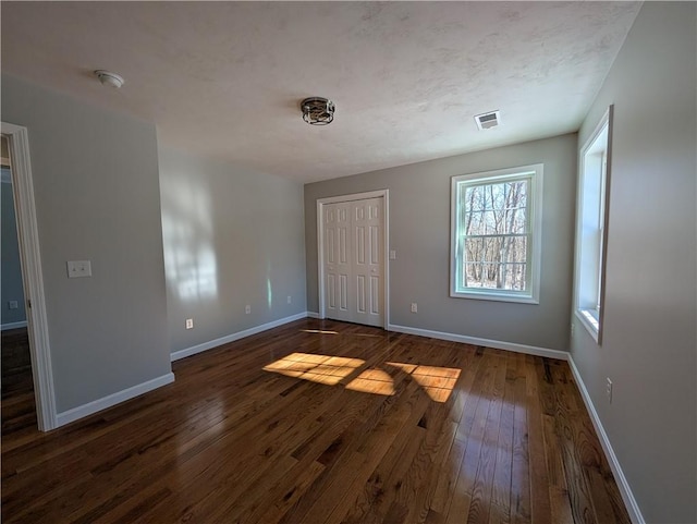 unfurnished bedroom with dark wood-style floors, a closet, visible vents, and baseboards