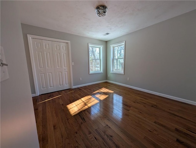 unfurnished bedroom with dark wood finished floors, a closet, visible vents, a textured ceiling, and baseboards