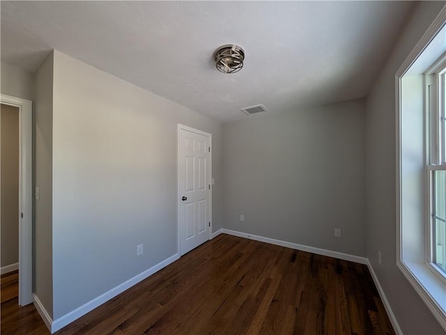 unfurnished room with dark wood-style floors, visible vents, and baseboards