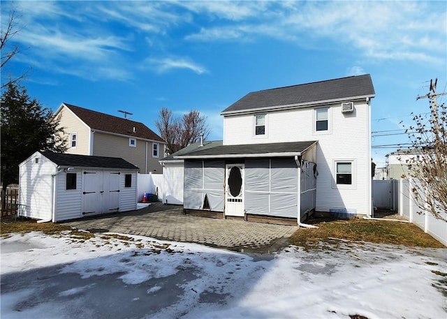 snow covered back of property with a shed, fence, and an outdoor structure