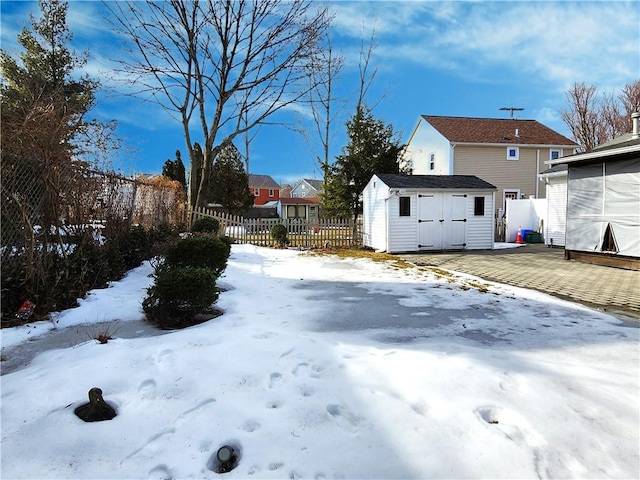 yard covered in snow featuring a storage unit, an outdoor structure, and fence