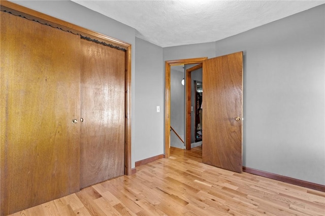 unfurnished bedroom with light wood finished floors, a textured ceiling, baseboards, and a closet