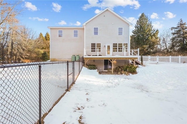 snow covered house with a fenced backyard and a deck