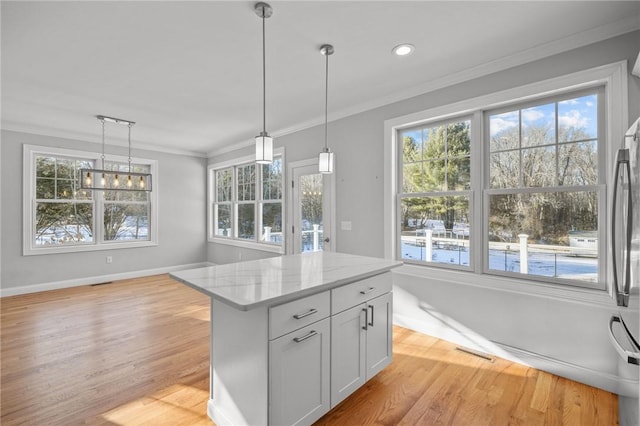 kitchen featuring white cabinets, ornamental molding, hanging light fixtures, light stone countertops, and light wood-type flooring