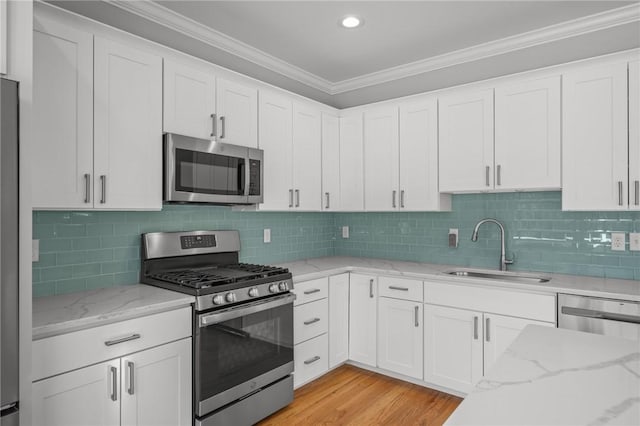 kitchen featuring light stone counters, stainless steel appliances, ornamental molding, white cabinets, and a sink