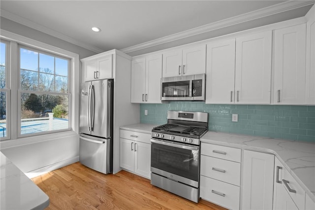 kitchen with light stone counters, crown molding, stainless steel appliances, white cabinetry, and light wood-type flooring