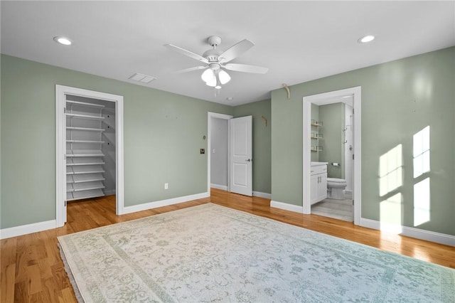 unfurnished bedroom with baseboards, a walk in closet, visible vents, and light wood-style floors