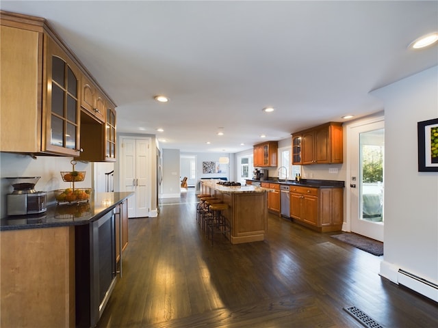 kitchen with a baseboard radiator, a kitchen breakfast bar, stainless steel dishwasher, brown cabinets, and glass insert cabinets