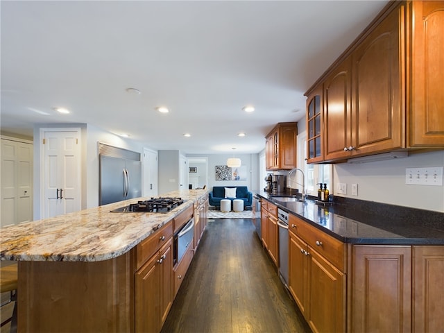 kitchen featuring stainless steel appliances, dark wood-type flooring, a sink, brown cabinets, and a warming drawer