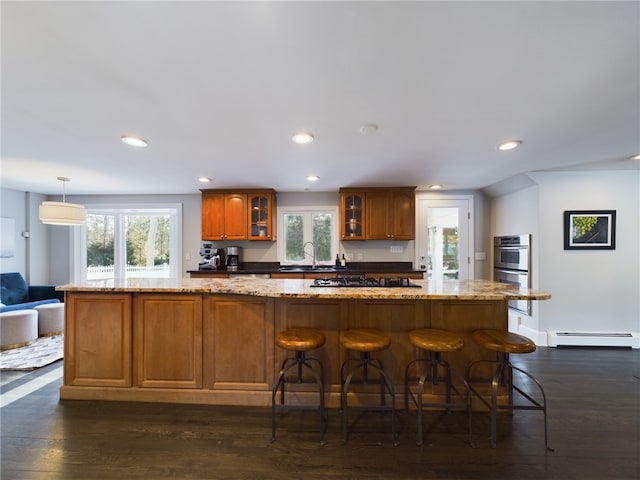 kitchen featuring dark wood-type flooring, a sink, baseboard heating, a wealth of natural light, and brown cabinetry